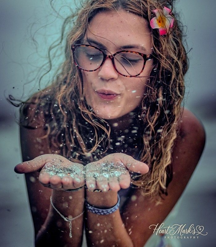 A young woman blowing glitter into the wind at the beach
